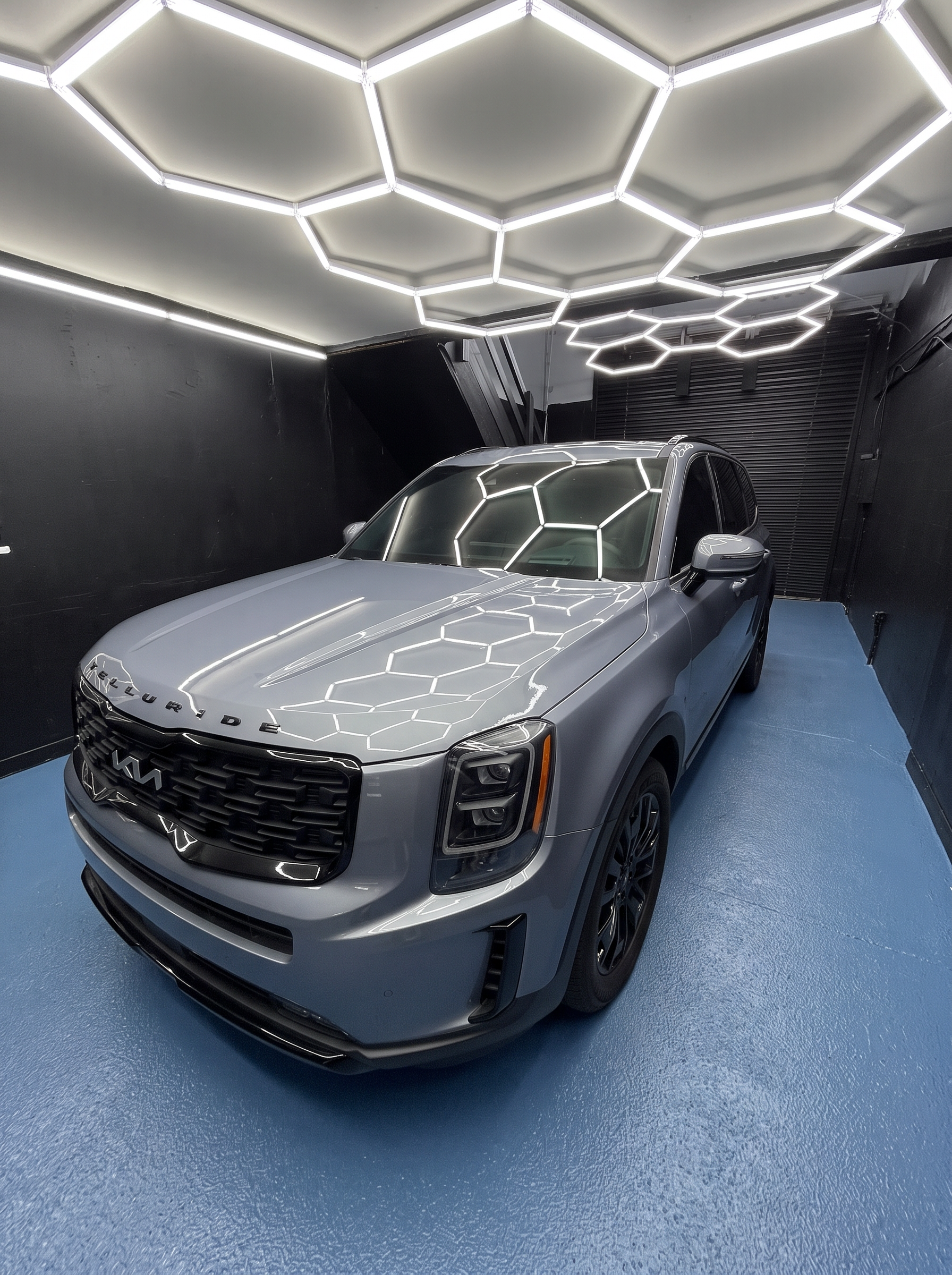 Gray Kia Telluride beneath the shop's inspection lights
